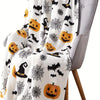 A white flannel throw blanket featuring a spooky Halloween print with black bats, spiders, and pumpkins draped over a gray ch