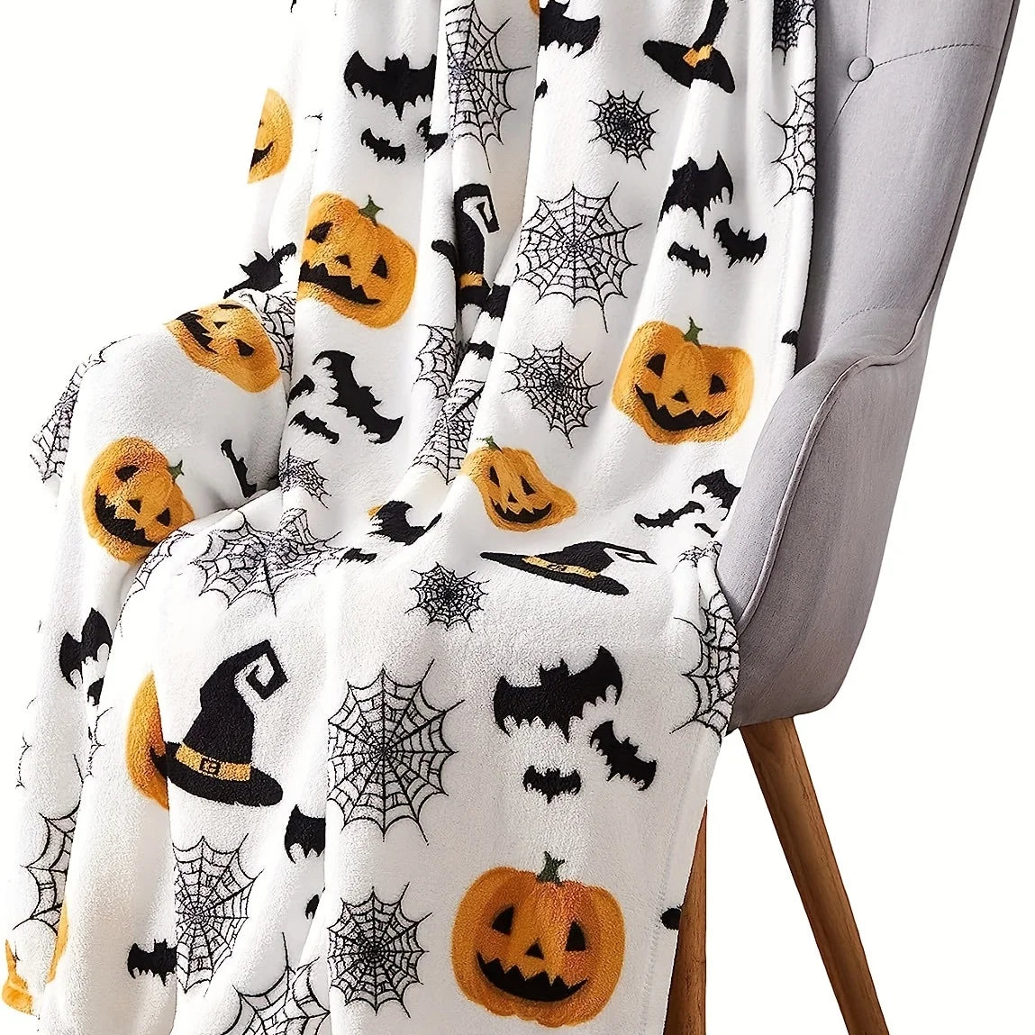 A white flannel throw blanket featuring a spooky Halloween print with black bats, spiders, and pumpkins draped over a gray ch