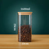 A clear glass storage canister with a bamboo lid filled with dark roasted coffee beans on a wooden surface.