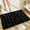 Black plush non-slip absorbent bathroom rug with pebble texture placed on a wooden floor.