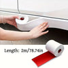 Hands are applying a roll of red self-adhesive PVC strip to protect a car's side skirt or door edge.
