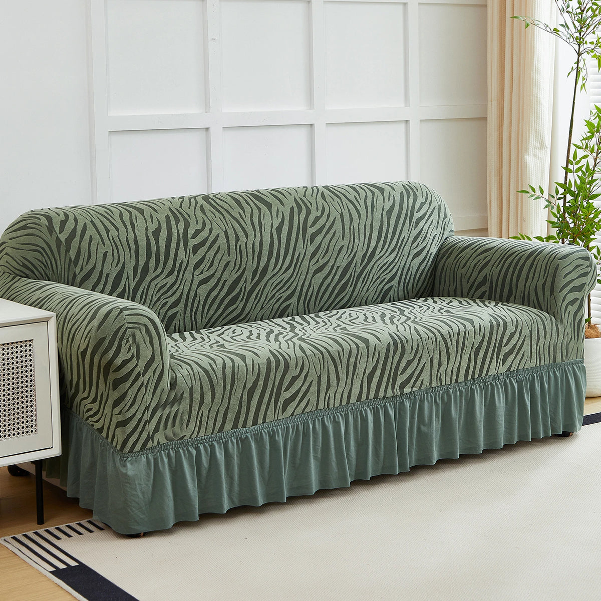 A teal jacquard sofa cover with a striped pattern and an elastic skirt displayed on a light rug.