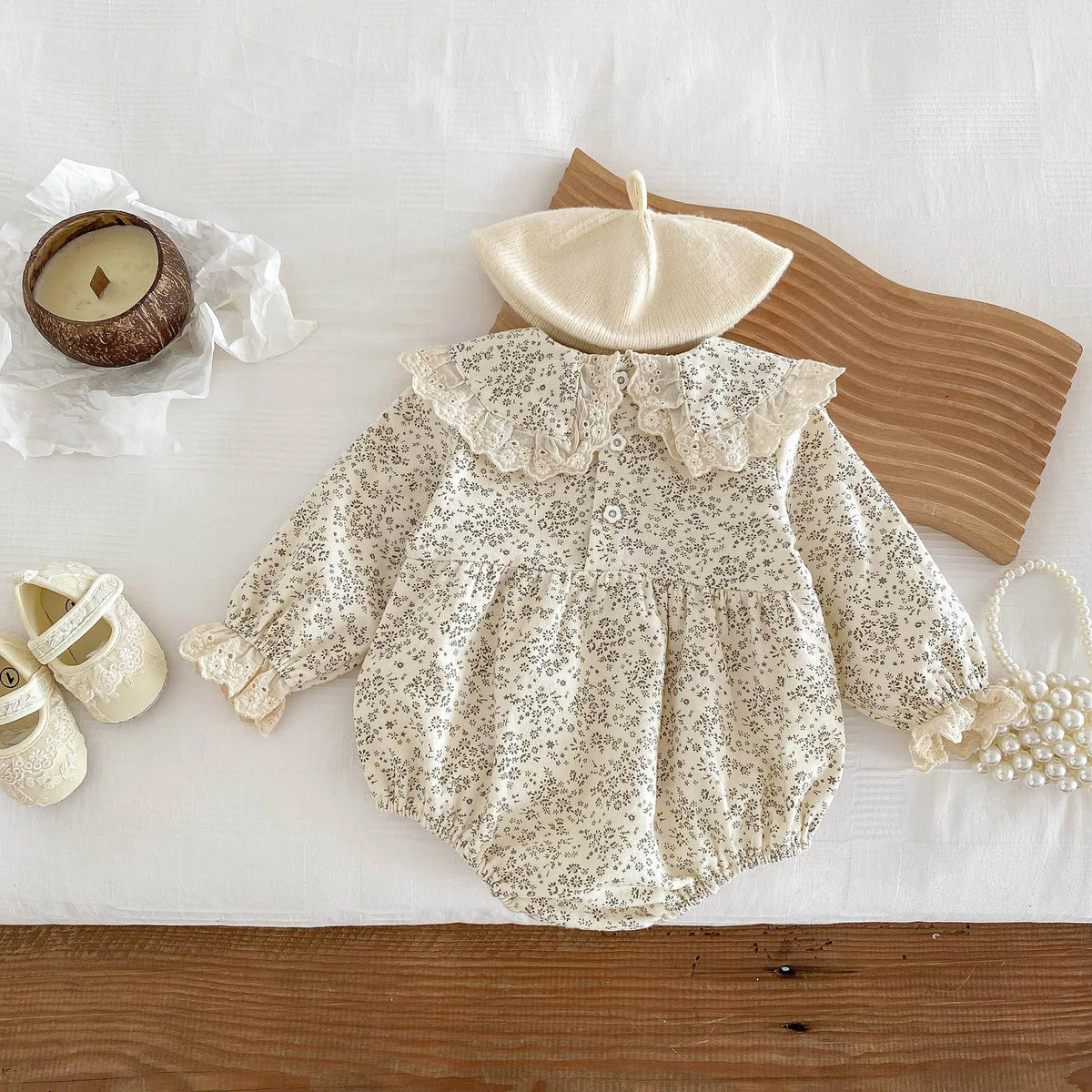 A cream floral lace cotton romper for a baby girl displayed on a white surface with natural wood accents.