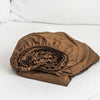 A rolled up brown linen fitted sheet with deep pockets resting on a white bed.