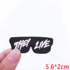 Black embroidered iron-on letter patch with the words THEY LIVE on a finger