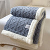 A gray fleece throw blanket with a white sherpa trim is folded on a white bed.
