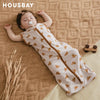 A baby wearing a beige breathable cotton sleep sack with adjustable sleeves lying on a brown textured blanket.