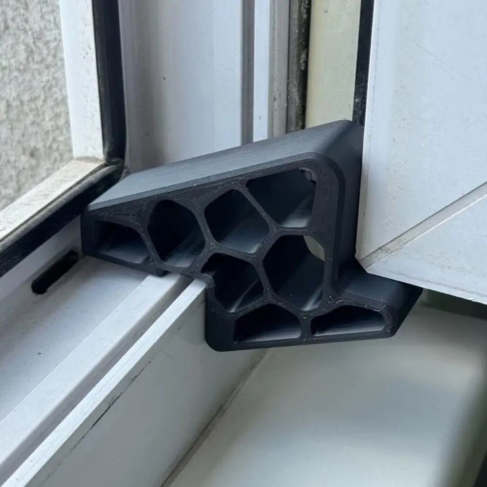 A black heavy-duty non-slip door stopper wedge is shown installed in a white window frame.
