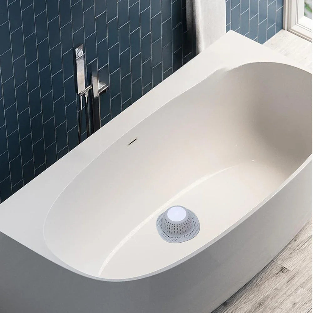 A white, oval bathtub features a circular silicone drain hair catcher installed on the side.