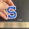 A hand holds a blue embroidered letter S patch, measuring 5.2 by 3.8 cm against a ruler.