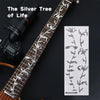 A close-up of a guitar fretboard featuring silver tree inlay stickers and a similar pattern on a sheet of paper.