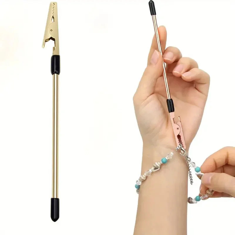 A hand holds a gold and black retractable bracelet fastening tool, demonstrating its use on a wrist.