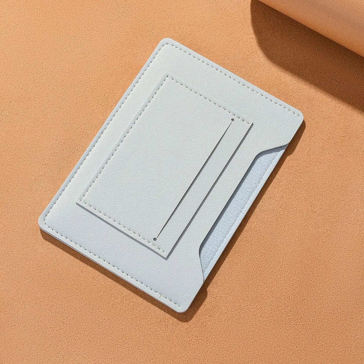 A light blue leather passport holder with card slots lying on a beige surface.