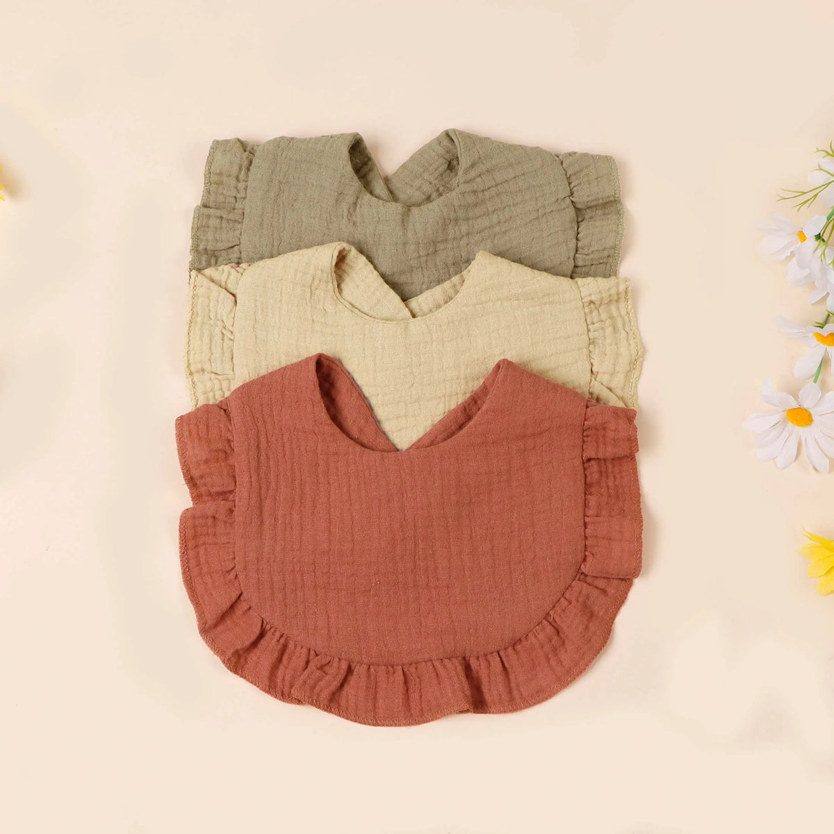 A set of three soft cotton ruffle bibs in shades of olive green, cream, and terracotta.