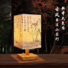 A wooden table lamp with a textured paper shade featuring traditional Chinese calligraphy and landscape painting.