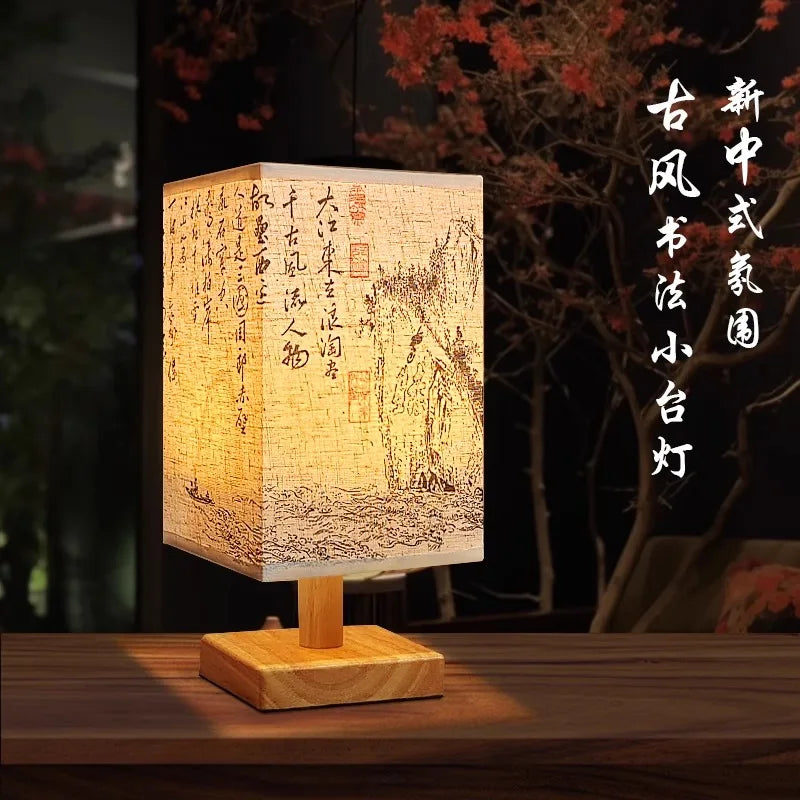 A wooden table lamp with a textured paper shade featuring traditional Chinese calligraphy and landscape painting.