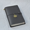 A dark gray leather refillable journal with a gold-toned watch attached to the cover.