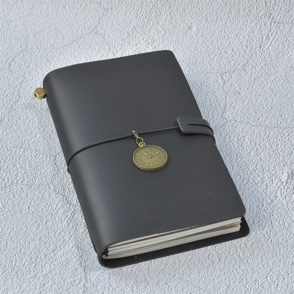 A dark gray leather refillable journal with a gold-toned watch attached to the cover.
