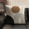 A beige linen cushion cover with a large circular brown design and black geometric lines on a dark sofa.