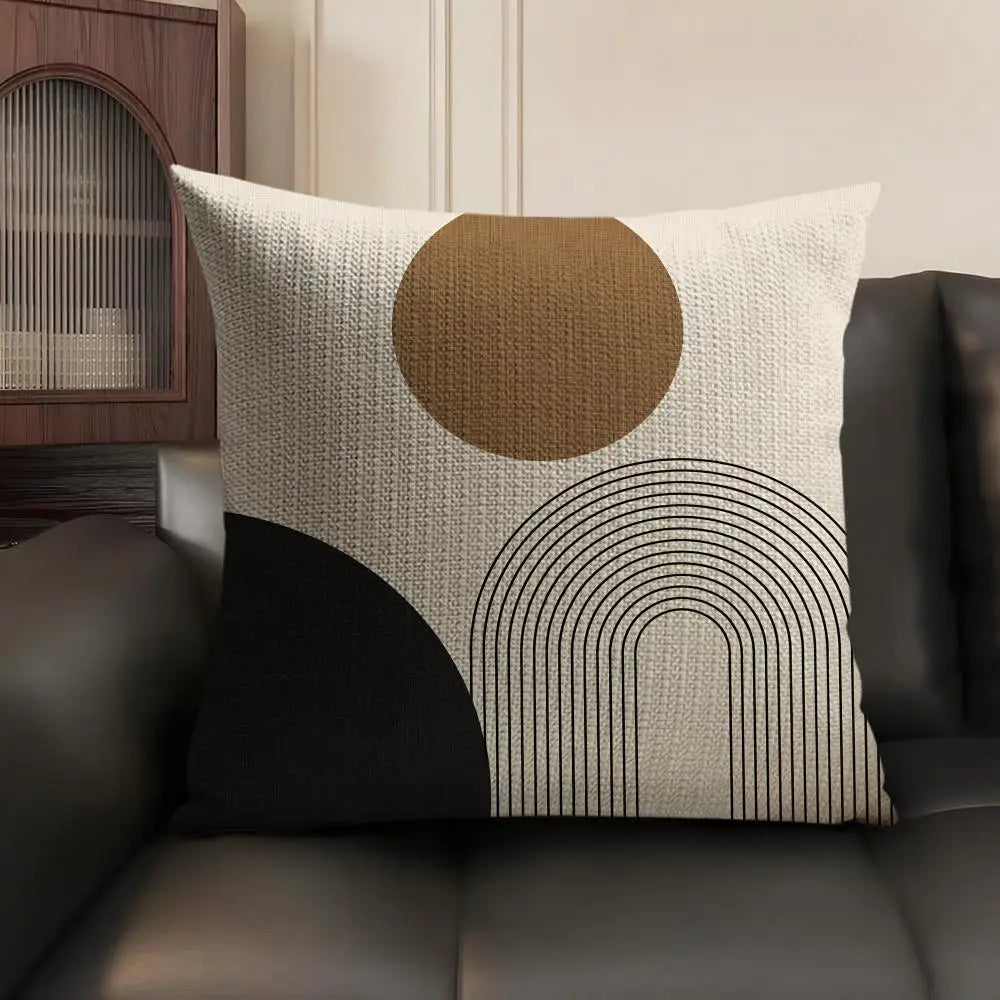 A beige linen cushion cover with a large circular brown design and black geometric lines on a dark sofa.