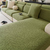 A moss green jacquard fleece sofa cover with an anti-slip backing and light cream pillows.