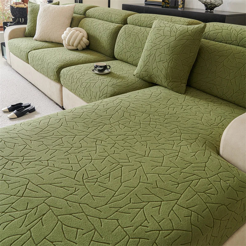 A moss green jacquard fleece sofa cover with an anti-slip backing and light cream pillows.