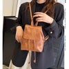 Une femme portant un blazer noir tient un mini sac à dos en cuir marron à cordon.