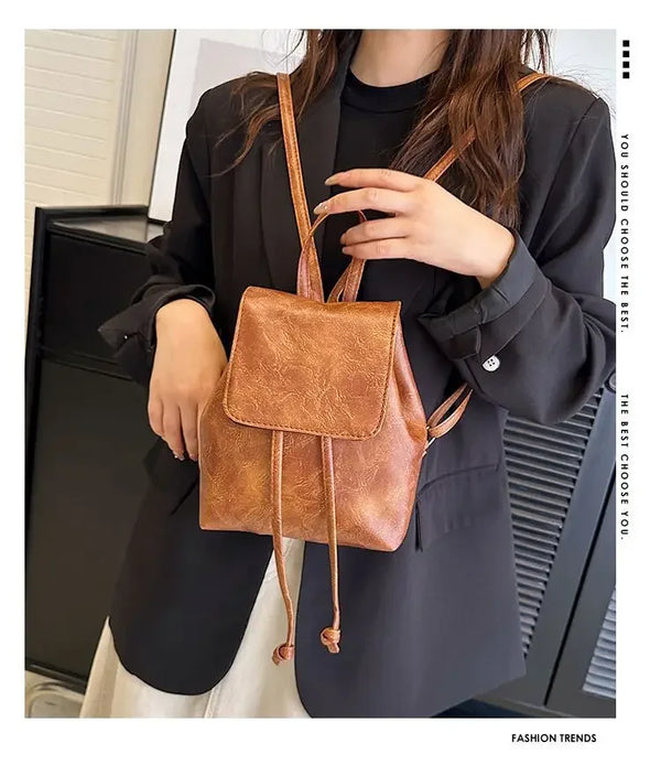 Une femme portant un blazer noir tient un mini sac à dos en cuir marron à cordon.