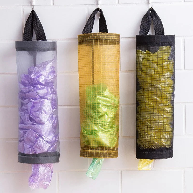 Three wall-mounted plastic bag dispensers filled with purple, green, and yellow bags.
