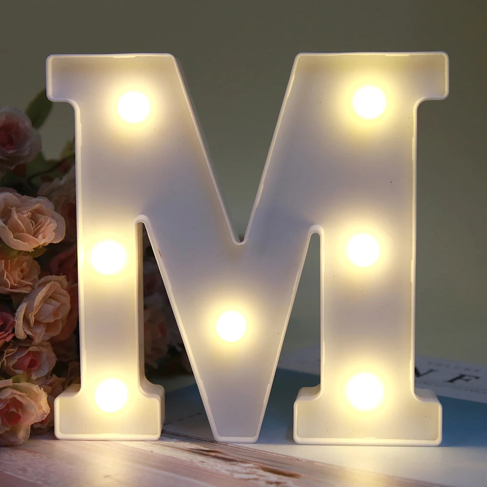 Lumière de nuit alphabétique LED blanche lumineuse en forme de lettre M, posée sur une surface en bois.