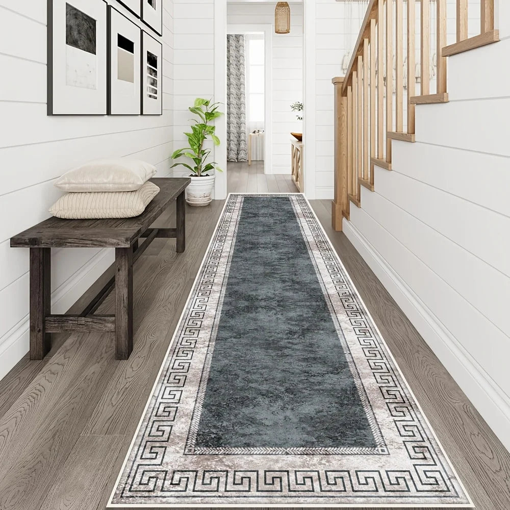A long runner rug with a geometric pattern in navy and grey is placed on a wooden floor next to a white wall and a wooden sta