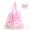 A pink reusable shopping tote bag with a matching pink carry pouch featuring a floral pattern.