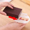 A hand is holding a dark brown heavy-duty emery sponge for pots and pans, demonstrating its texture.