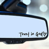 A close-up view of a clear vinyl sticker with the text Trust in God and a heart symbol on a dark surface.