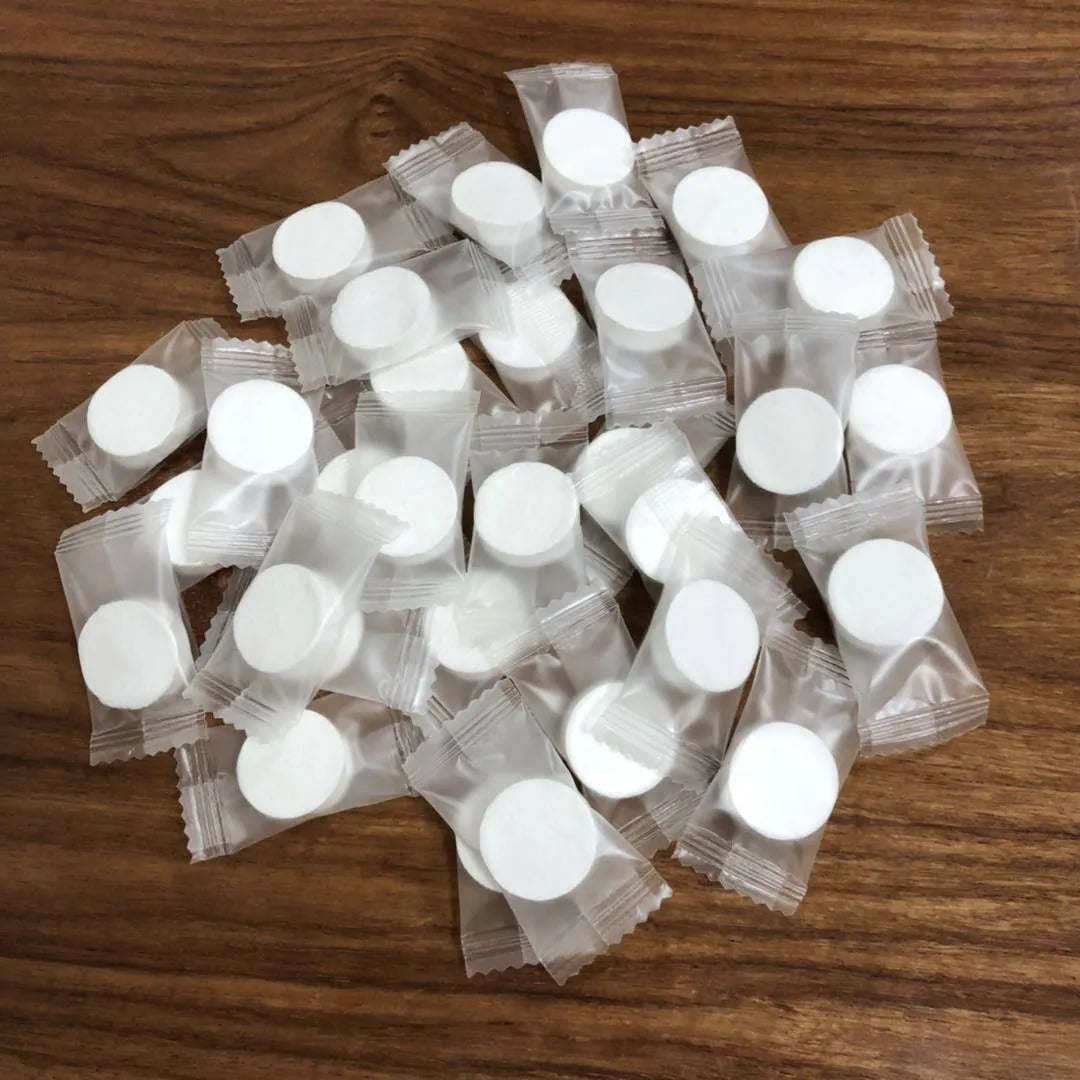 A pile of white portable compressed cleansing towels packaged in clear plastic pouches on a wooden surface.