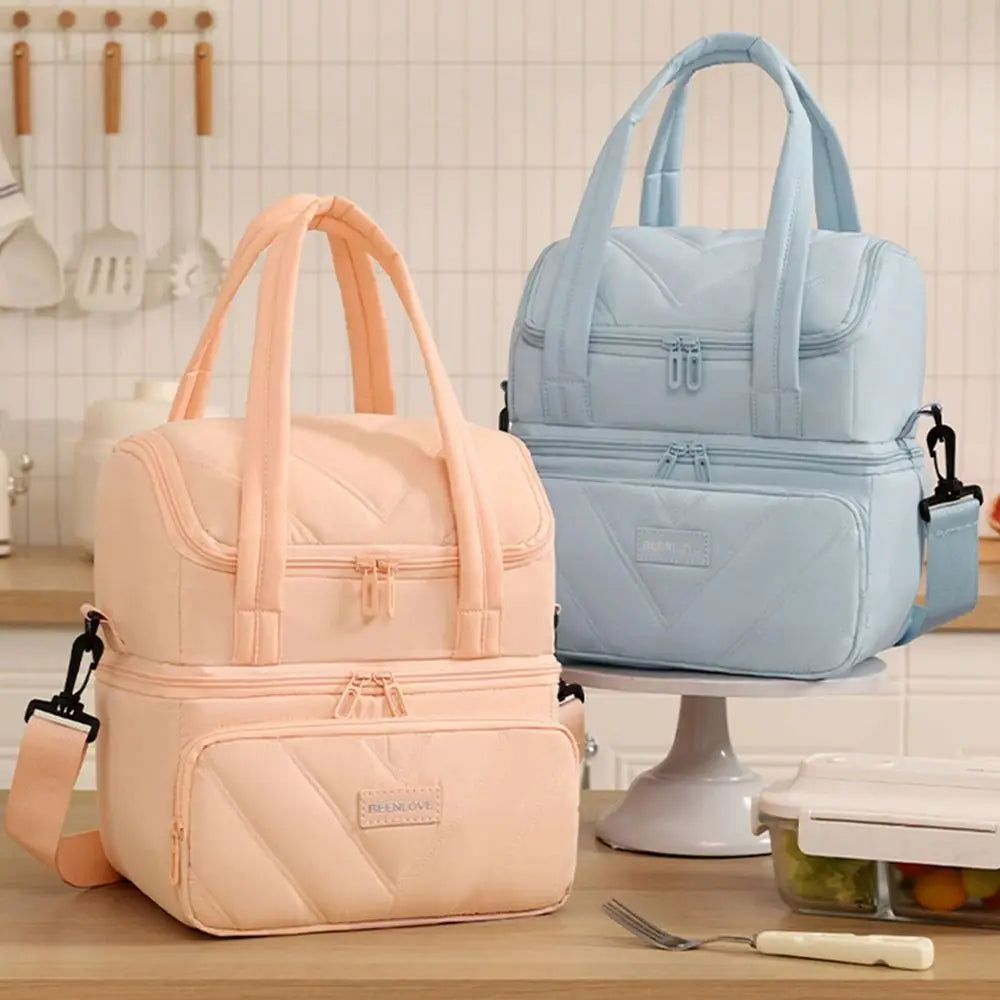 A light pink insulated reusable lunch bag and a light blue insulated reusable lunch bag are displayed on a table.