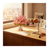 A pink cherry blossom bouquet in a glass vase sits on a wooden table next to framed photos.