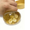 A hand is holding a clear, golden squishy dumpling fidget toy with small, textured balls inside, next to a yellow container.