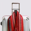 A red and striped reusable elastic luggage strap is shown draped over a silver suitcase.