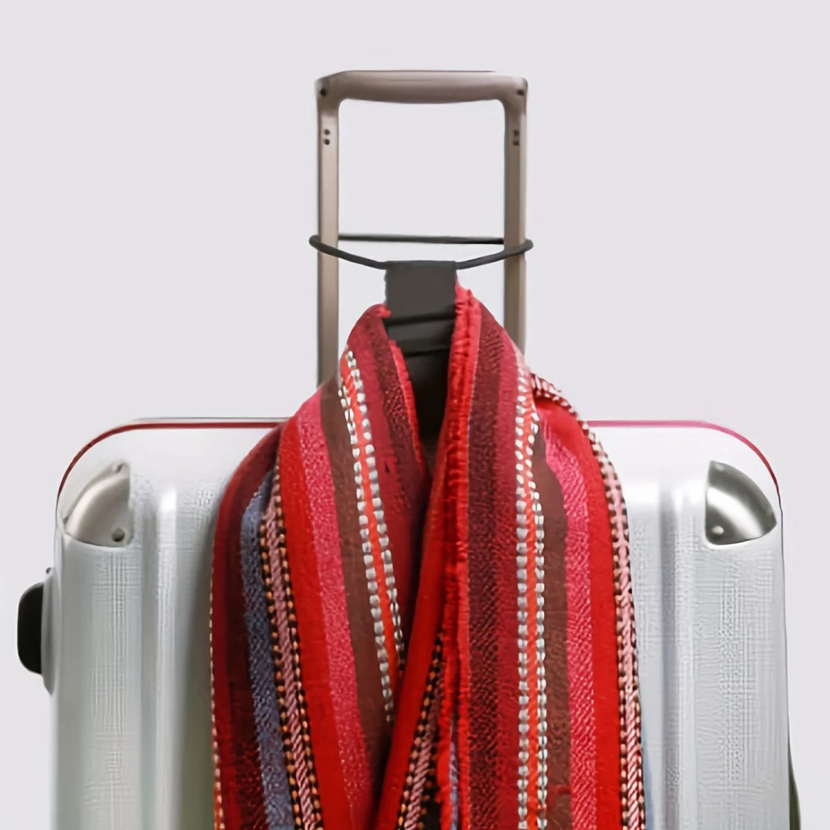 A red and striped reusable elastic luggage strap is shown draped over a silver suitcase.