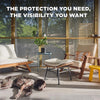 A living room scene showing a dog resting on the floor near wooden furniture and large glass windows with a mesh screen visib