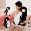 A woman is holding a black and white penguin plush toy in her arms, sitting on a light-colored sofa.