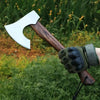 A hand-forged Viking tomahawk axe with a white blade and dark wooden handle is shown resting on green grass.