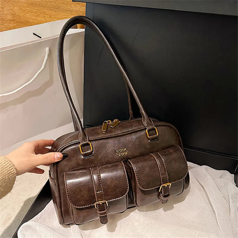 Braune Umhängetasche mit mehreren Taschen wird von einer Hand vor dunklem Hintergrund gehalten.