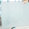 A close-up of frosted privacy window film with a stripe pattern being held by a hand.