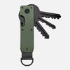 A minimalist aluminum key organizer in olive green holds several metal keys.