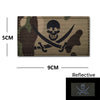 A dark camouflage embroidered patch featuring a skull and crossed swords design with reflective accents.