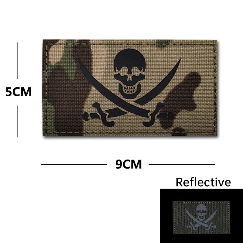 A dark camouflage embroidered patch featuring a skull and crossed swords design with reflective accents.