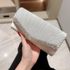 A hand holds an elegant white patent leather clutch bag with a silver chain strap.