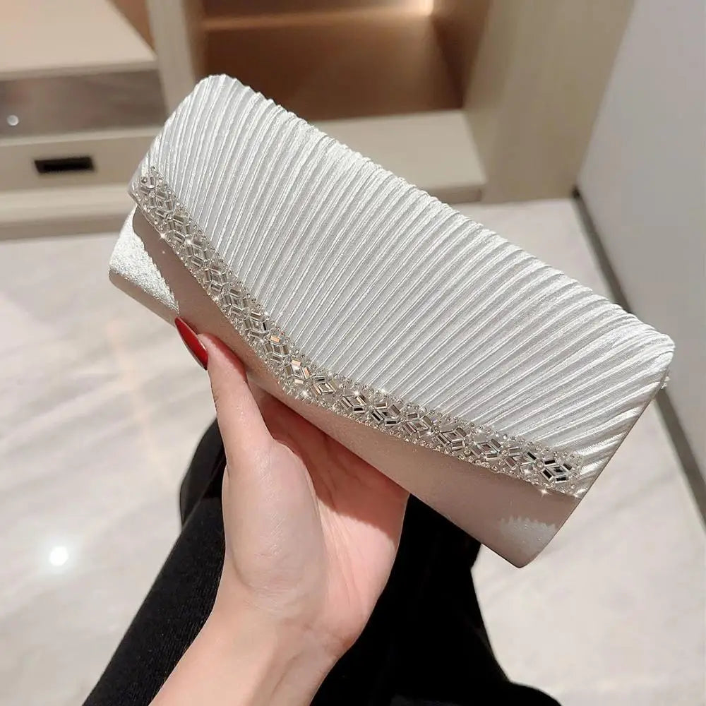 A hand holds an elegant white patent leather clutch bag with a silver chain strap.